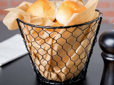Black chicken wire basket contains yellow paper and bread.