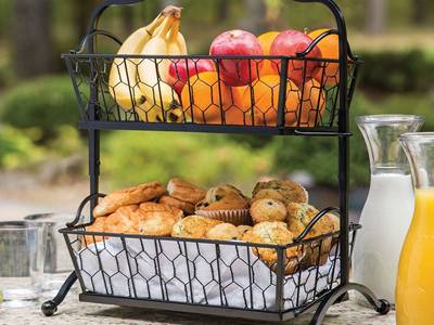 A two levels chicken wire mesh made basket is placed, with fruit on the top level, bread on the lower level.