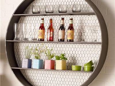 A round shelf has wine, cups and plants inside.