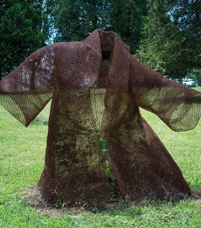A rusty chicken wire mesh made coat is placed in a some forest like place.